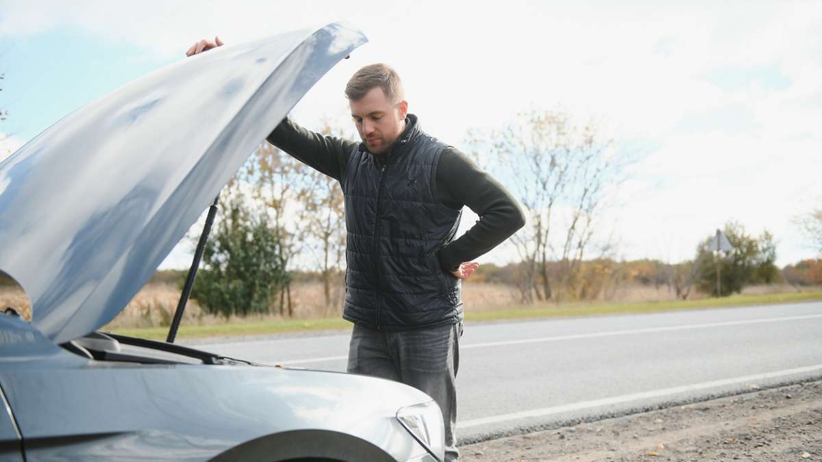 jeune homme vérifiant sa voiture en panne sur le bord de la route