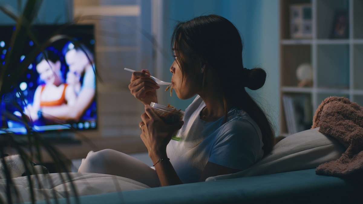 jeune femme mangeant sur le canapé devant la télévision