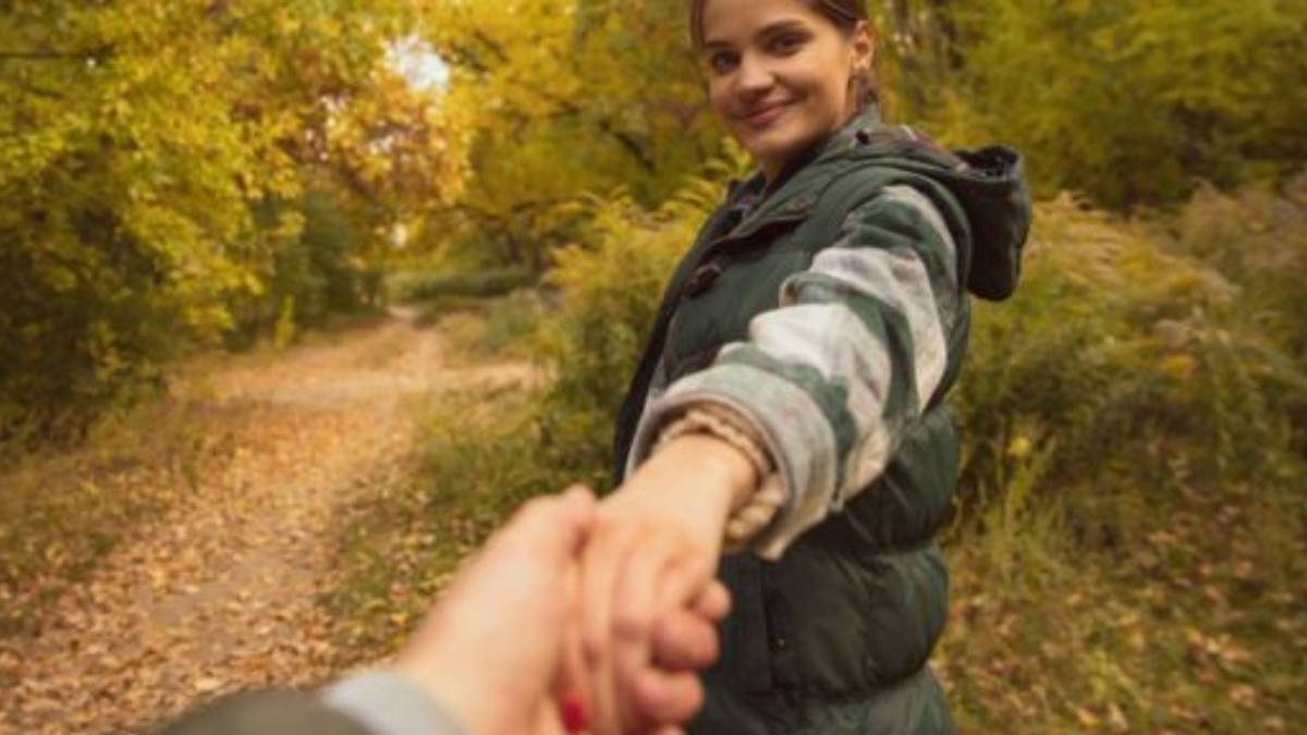 femme tournée vers son ami qu'elle tient par le bras pour le guider dans les bois