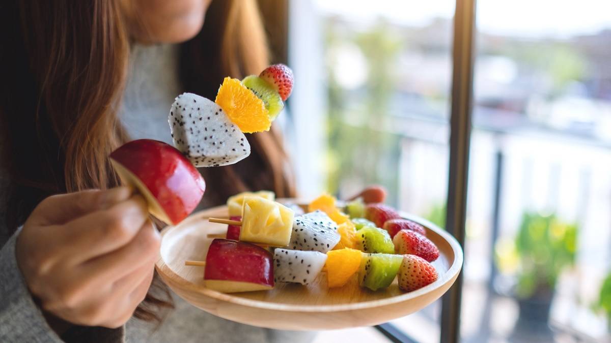 jeune femme mangeant des fruits sur une brochette