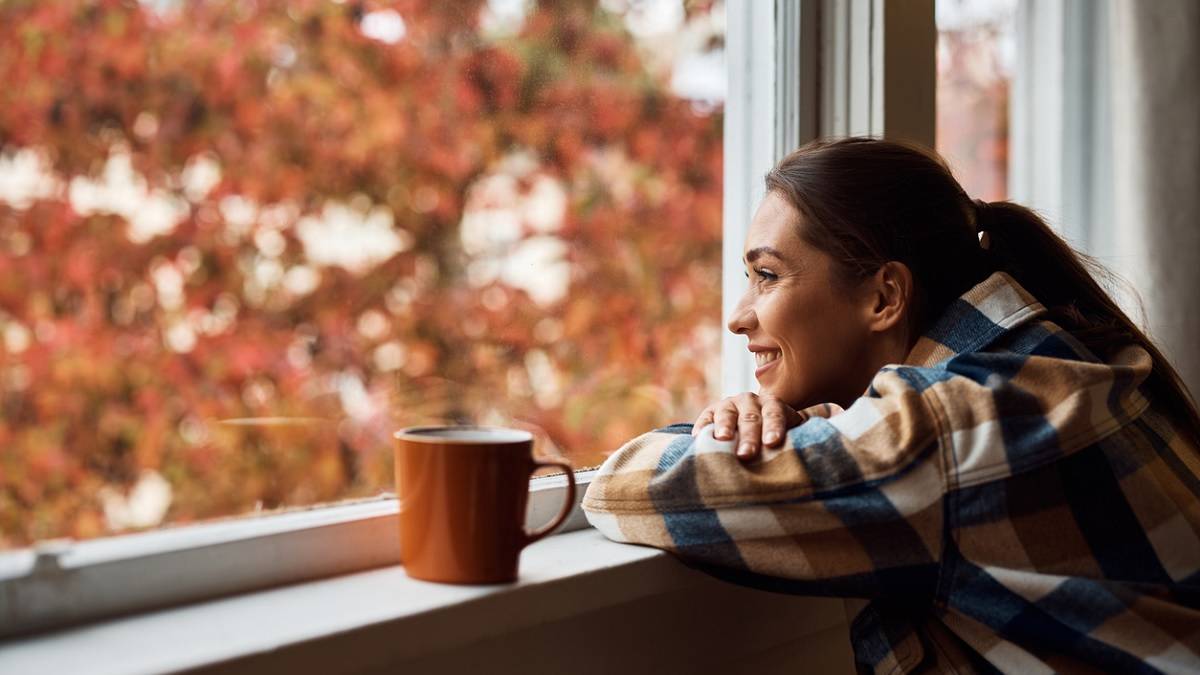 jeune femme heureuse regardant par la fenêtre en automne