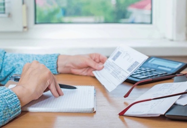 Une femme assise à une table examinant les factures sur une calculatrice