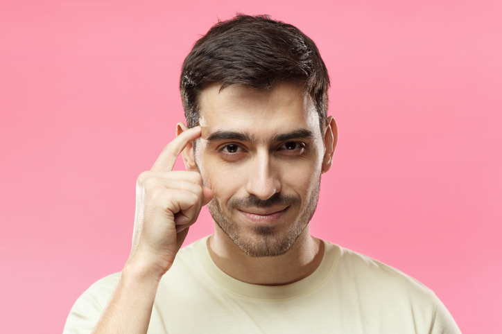 Jeune homme souriant qui désigne son cerveau avec le doigt