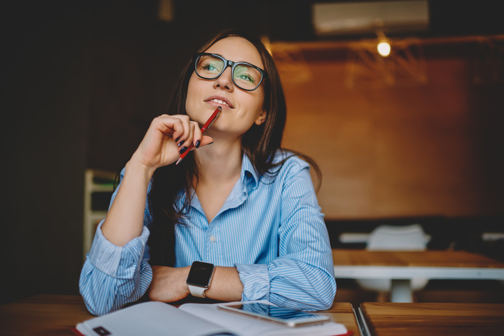 Une jeune femme, qui porte des lunettes, réfléchit en esquissant un rictus 