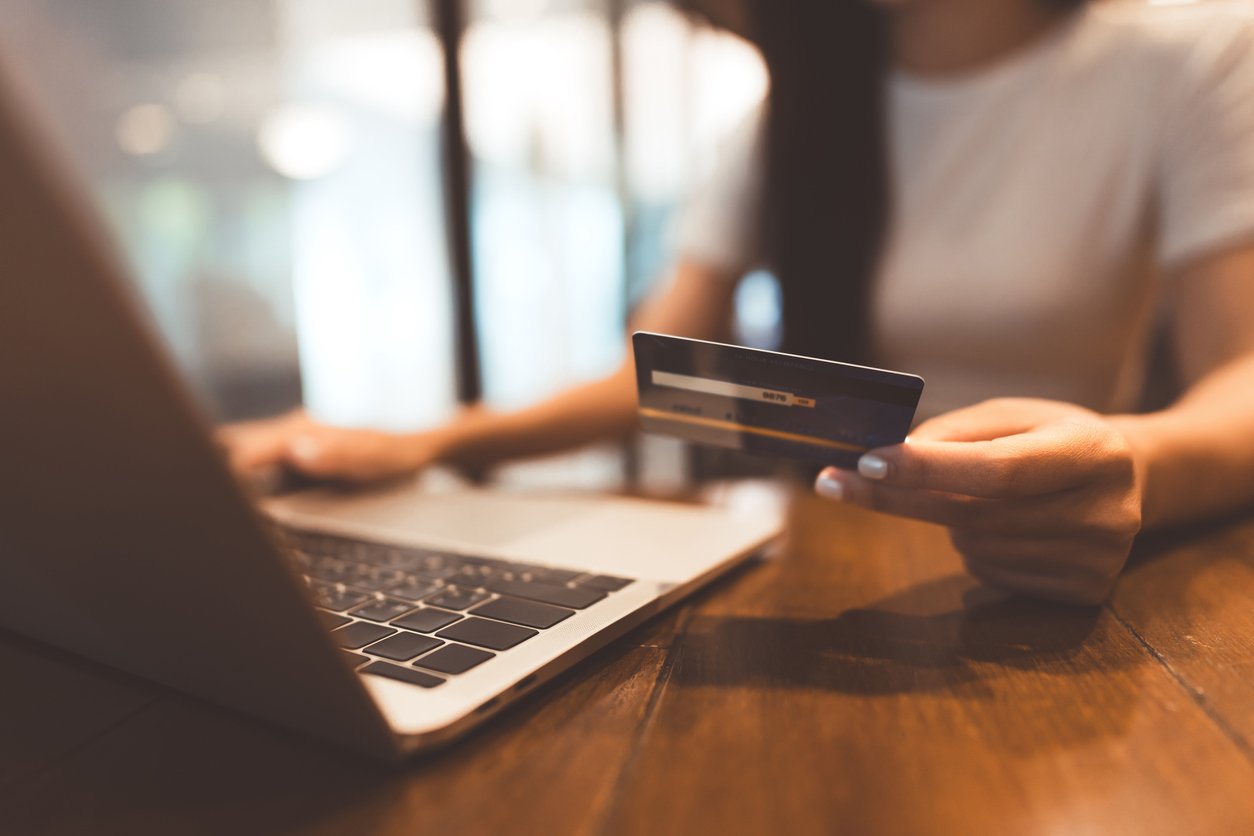 Une femme sort sa carte bancaire devant son ordinateur