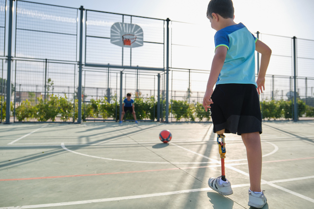 Un petit garçon portant une prothèse en train de jouer au football avec un ami