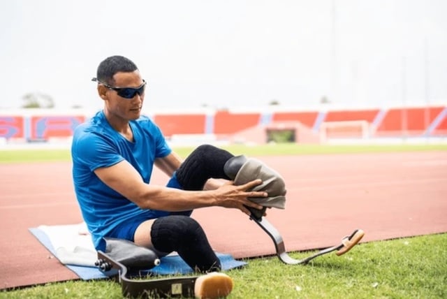 Un para-athlète asiatique avec des lames prothétiques s'étirant la jambe dans un stade