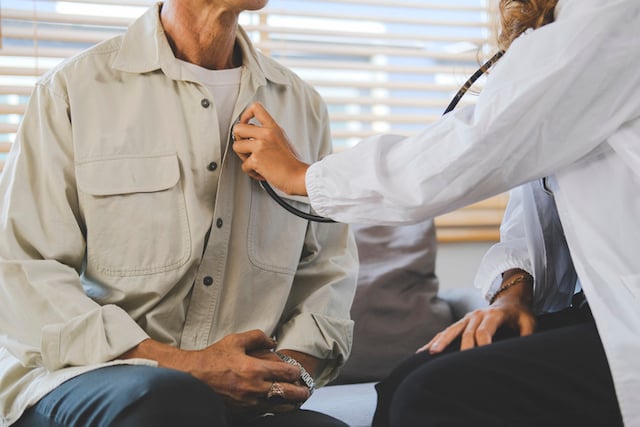 Une médecin tenant un stéthoscope écoute le cœur d’un patient âgé