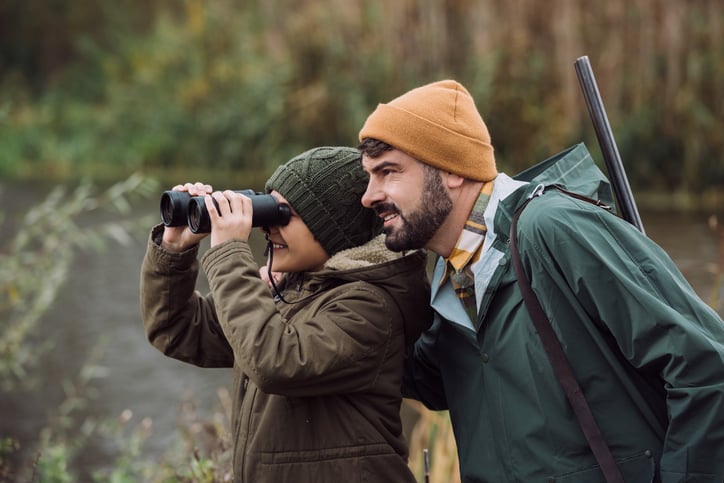 Un enfant regarde dans des jumelles avec son père chasseur