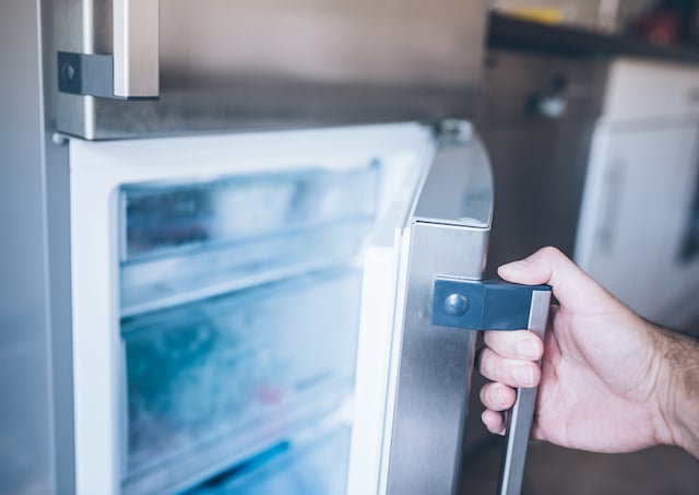 Un homme en train d'ouvrir la porte du congélateur dans la cuisine