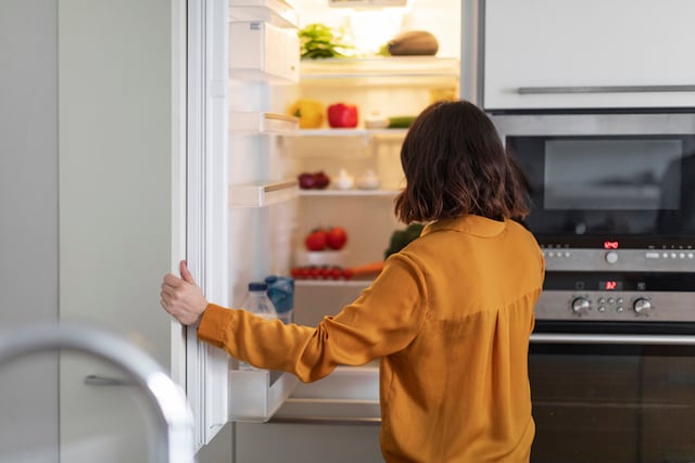 Un jeune femme ouvrant un réfrigérateur dans la cuisine