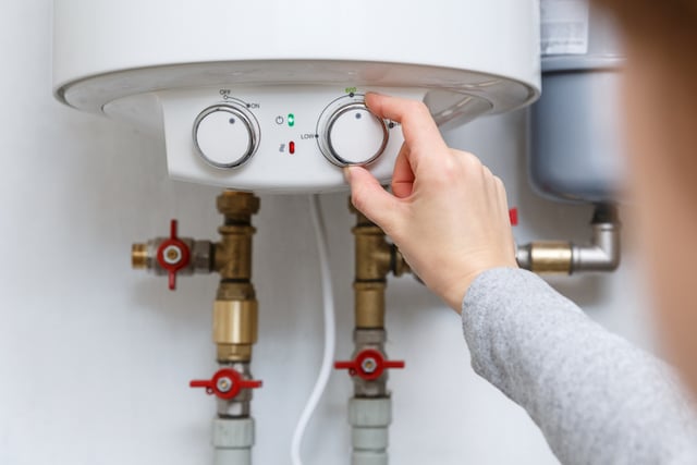 Une femme en train de régler thermostat de son ballon d'eau chaude électrique