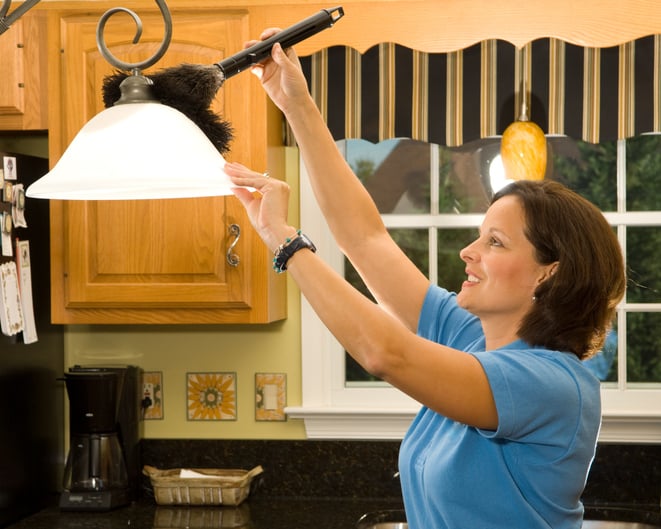 Une femme nettoie un luminaire avec un plumeau