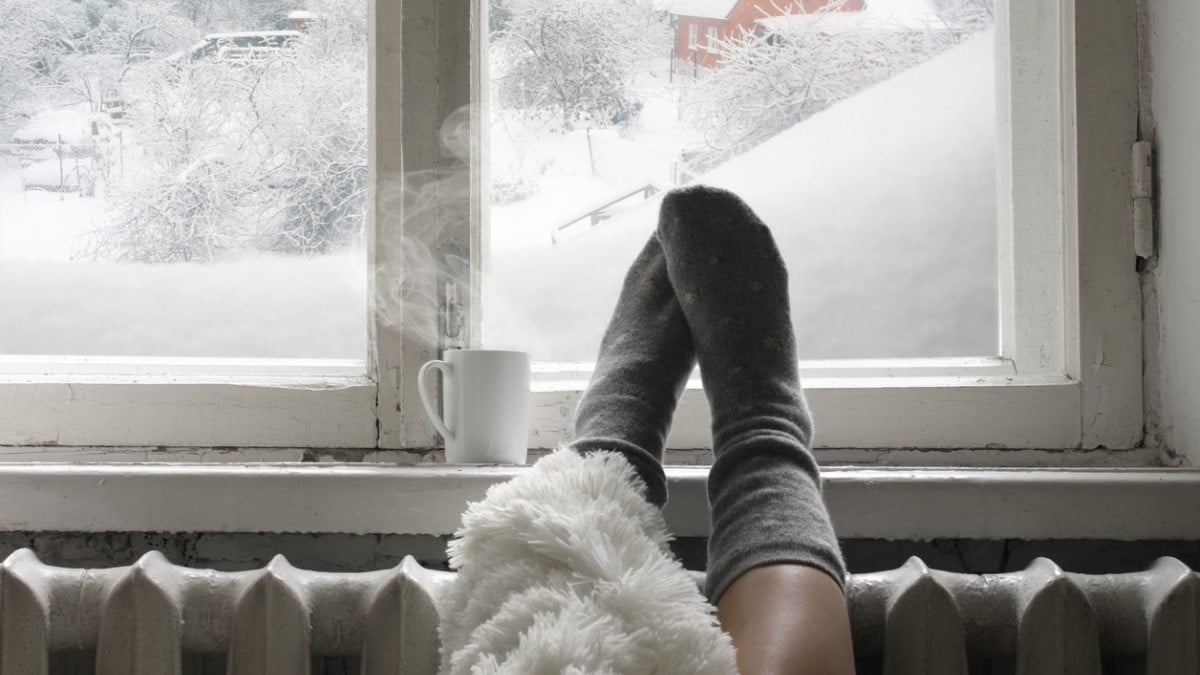 Une personne en chaussettes sur un radiateur avec une boisson chaude