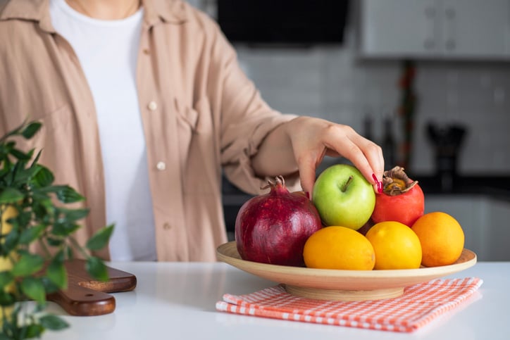 Une personne prend une pomme dans une corbeille à fruits