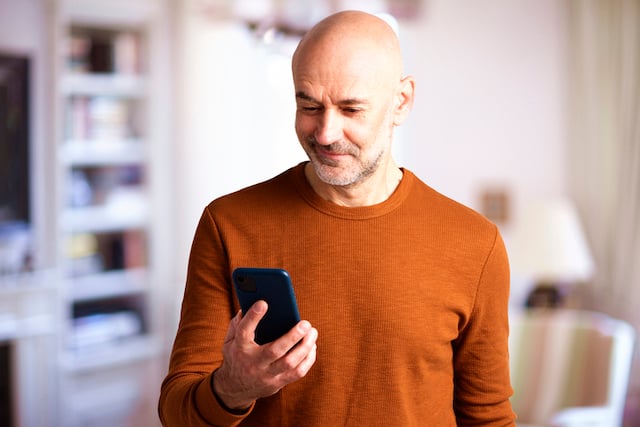 Un homme âgé d'une soixantaine d'années qui regarde son téléphone portable en souriant 