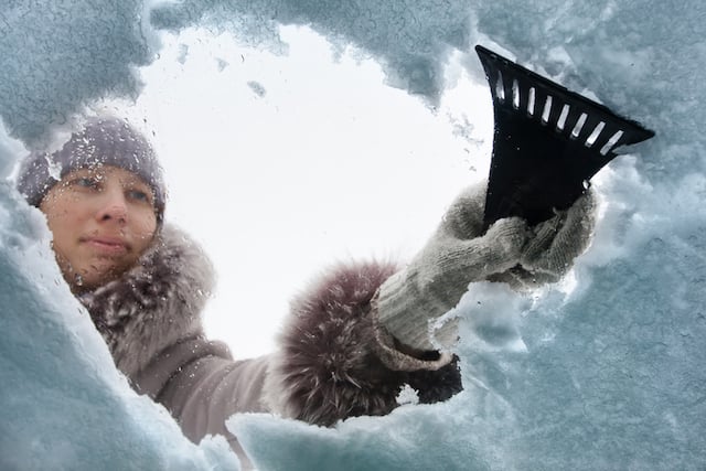 Une femme en train retirer la neige de son pare-brise