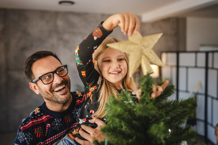 Une enfant et son père mettent une étoile en haut du sapin