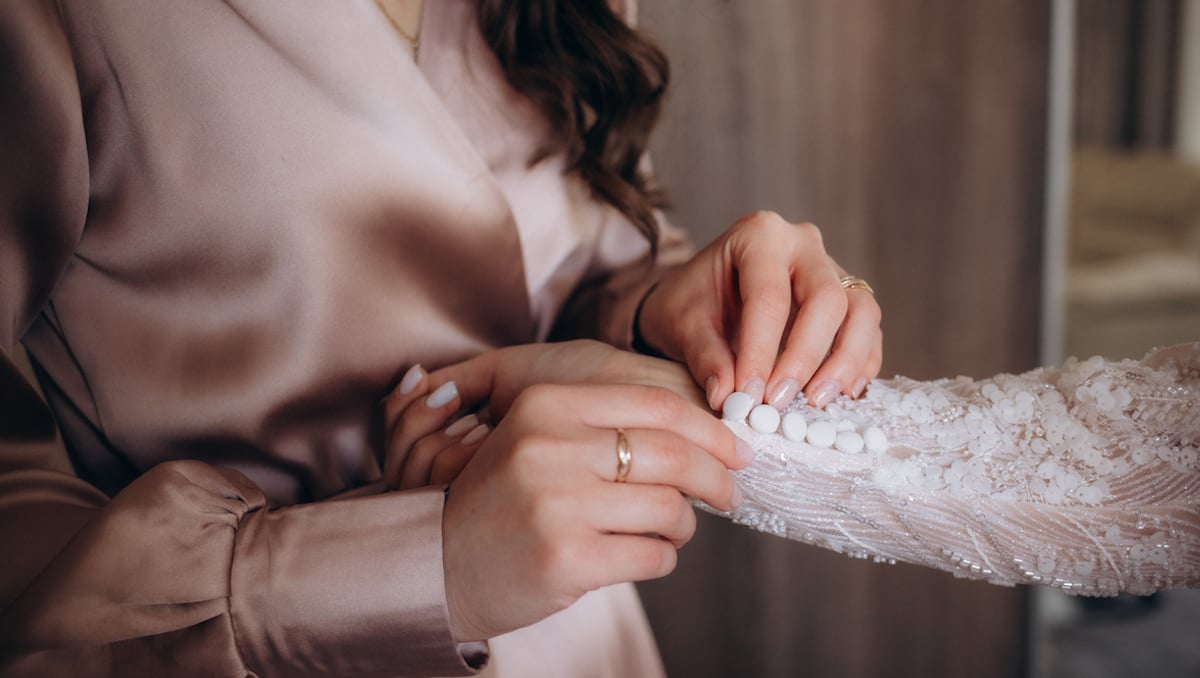 Une femme en train de boutonner la manche de la mariée