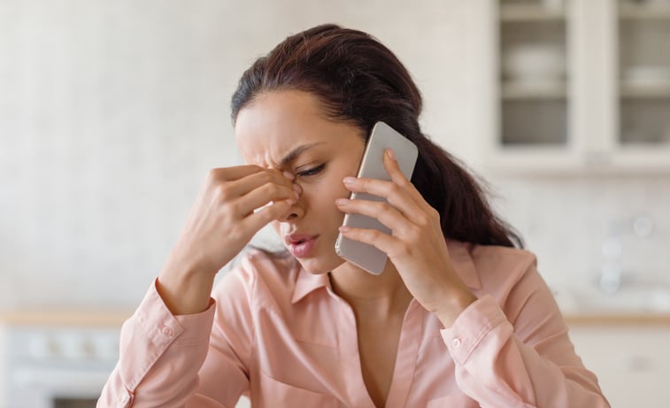 Une femme se pince le nez au téléphone