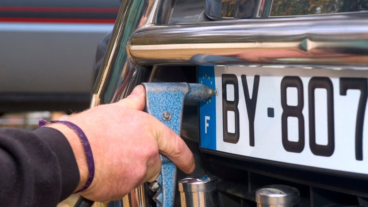 Un homme pose une plaque d'immatriculation sur un véhicule