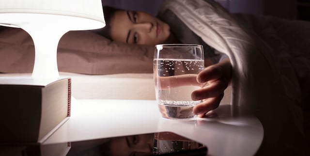 Une femme qui attrape un verre d'eau sur sa table de chevet