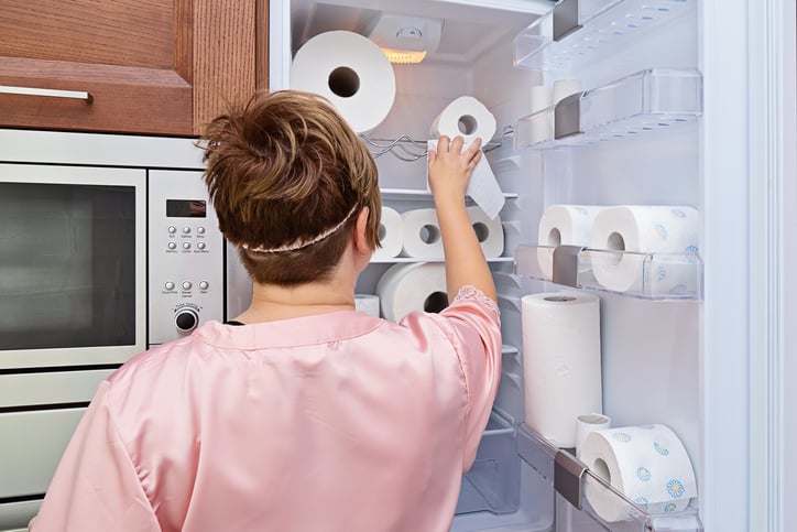 Une femme met des rouleaux de papier toilette dans un frigidaire 