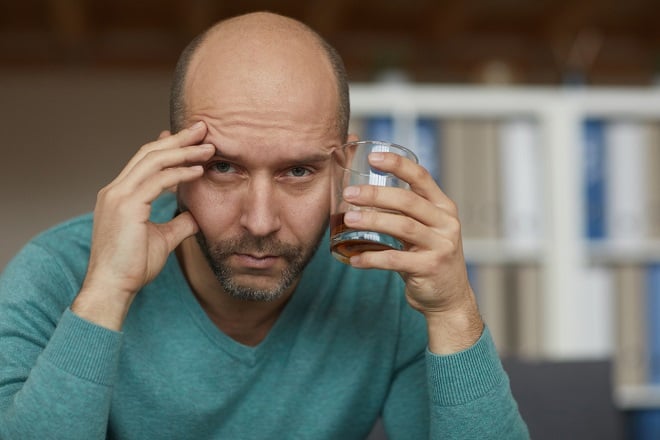 homme chauve avec un verre d'alcool dans les mains