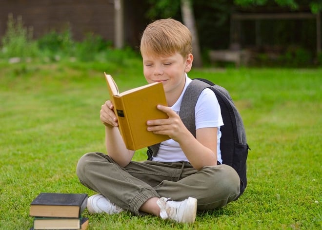 jeune garçon lisant tranquillement un livre assis sur une pelouse