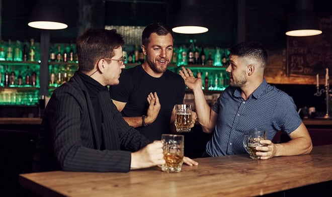 trois amis discutant avec un verre à la main dans un bar