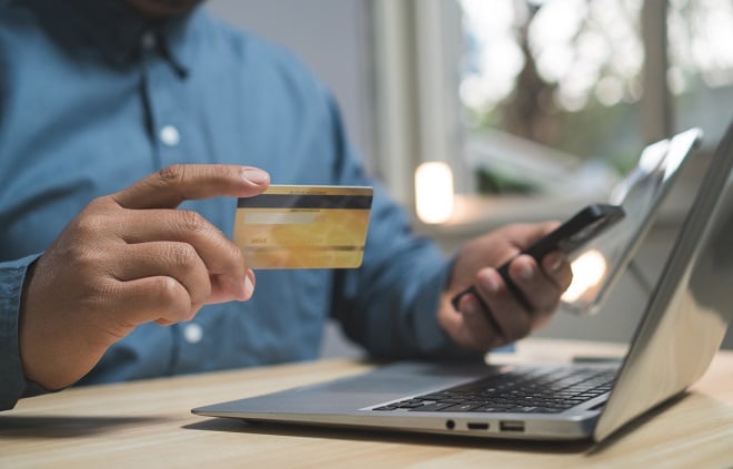 Homme tenant sa carte de crédit devant son ordinateur