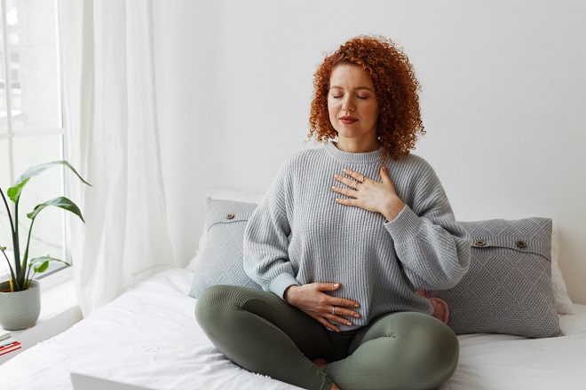 jeune femme assise sur son lit pratiquant un exercice de respiration