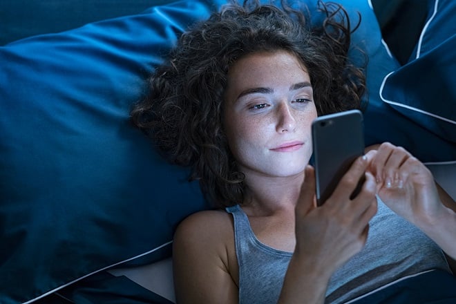 jeune femme réveillée regardant son smartphone la nuit