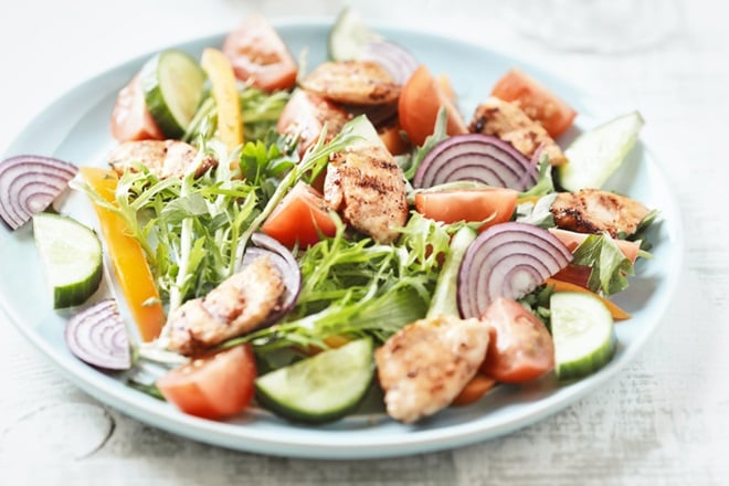 Assiette de salade au poulet, oignons rouges et crudités.