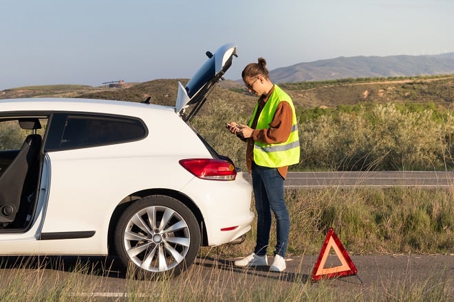 Homme portant un gilet fluo à côté d'un triangle rouge et de sa voiture en panne