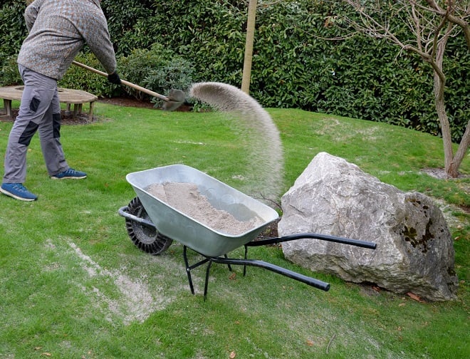 jardinier appliquant du sable blanc sur la pelouse verdoyante