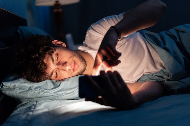 jeune homme scrollant sur son smartphone dans son lit