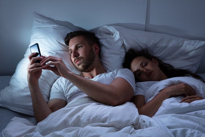 Homme regardant son téléphone au lit pendant que sa femme dort