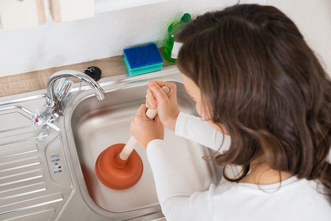 femme tentant de déboucher un évier avec une ventouse